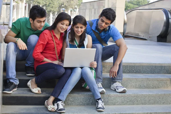 Group of happy friends surfing net while sitting on steps