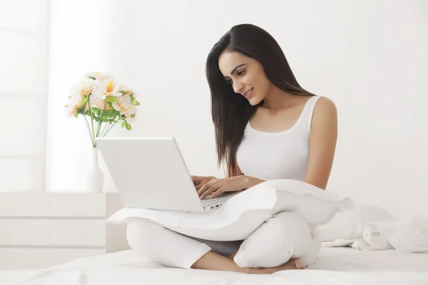 Indian woman using laptop on bed