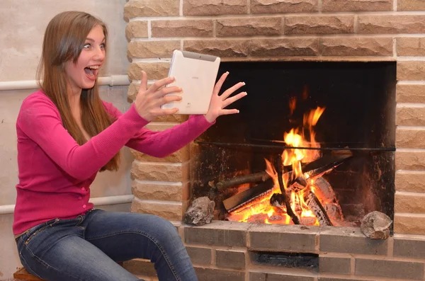 The girl is sitting alone near the fireplace and holds in hands the e-book tablet