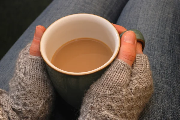 A woman in a cosy jumper holds a cup of tea or coffee on her lap
