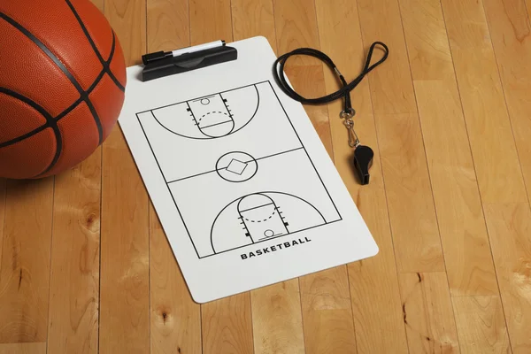 Basketball with coach's clipboard and whistle on wooden floor