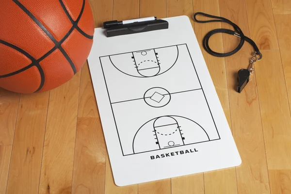 A basketball with coach\'s clipboard and whistle on a wooden gymn