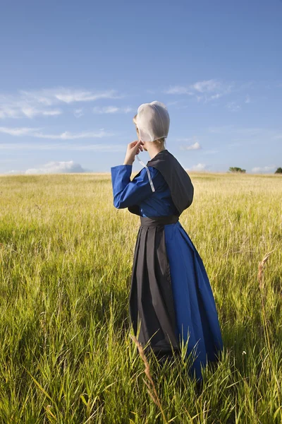 Amish woman standing in grassy field with afternoon sunlight