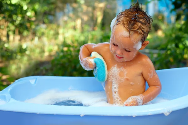 Baby boy washes with sponge in bubble bath outdoor