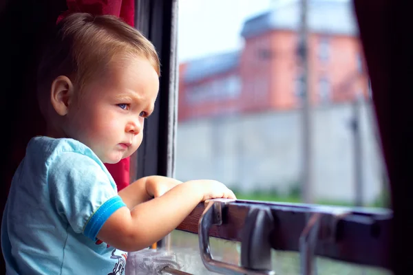 Cute little boy picking out from train window outside, while it moving