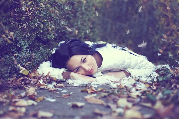 Mystic lonely angel girl lying on the ground among the fallen leaves and fe