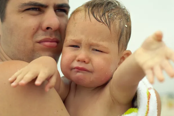 Upset little baby boy crying, stretching hands. with father outdoors