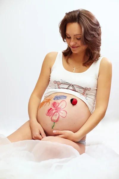 Beautiful pregnant woman looks at her painted and decorated belly. isolated