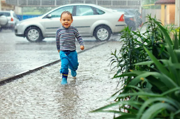 Cute baby boy running under the driving rain