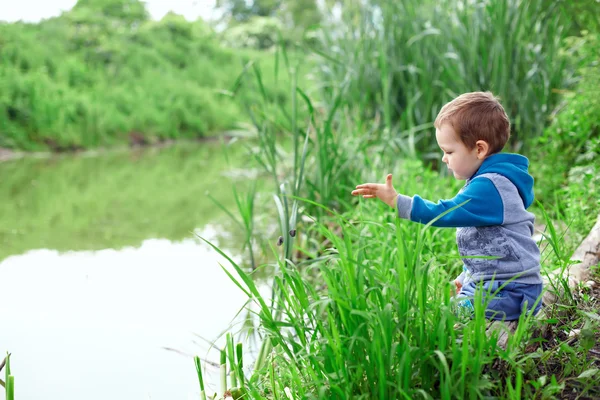 Lonely little boy sitting in cane on riverside, throwing stones