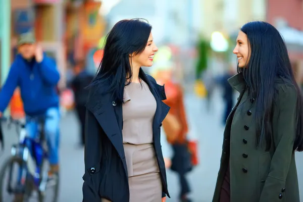 Two happy women talking on crowded city street