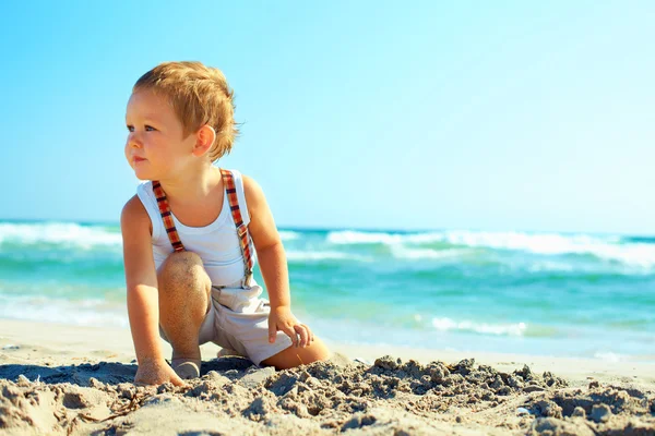 Thoughtful baby boy sitting on the beach