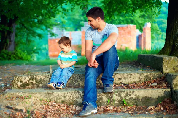 Father and son talk, while sitting on old stairs among trees
