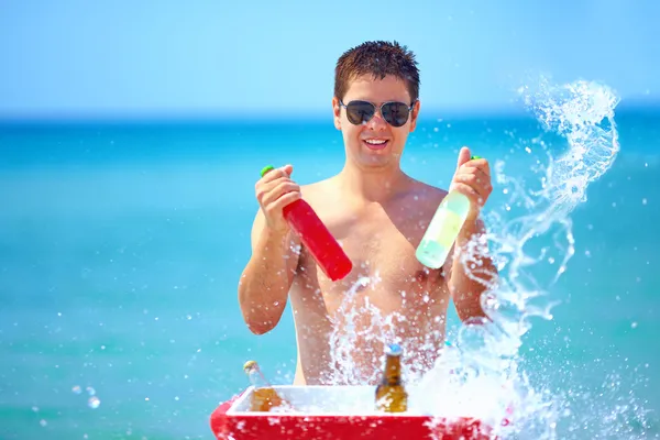 Happy man with drinks and water splash on the beach party