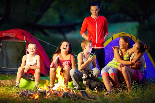 Happy kids telling interesting stories around campfire
