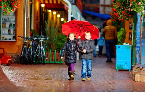 Cute children walking colorful evening street, under the rain