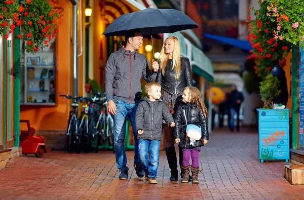 Happy family walking under the rain on cozy colorful street