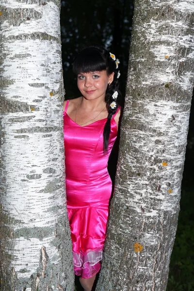 The smiling girl at a birch intertwined with daisies in her hair