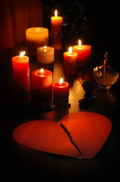 Romantic love letter in shape of broken heart (teared paper) with candles and old perfume bottle and pen.