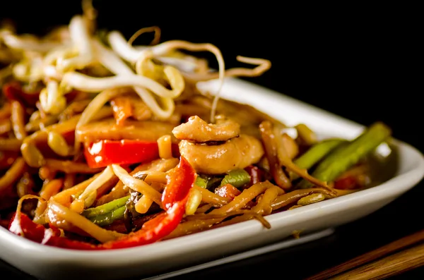 Stir-fried chinese noodles with chicken, vegetables and beansprouts on black