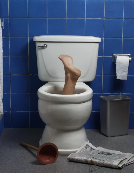 Foot reaches up through the seat from out of a toilet in a domestic bathroom.