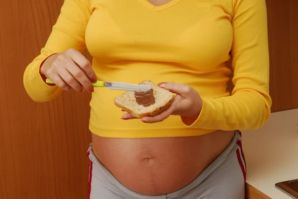 Young pregnant woman prepares a sandwich in a kitchen.