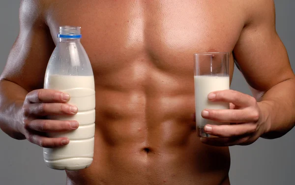 Shaped and healthy body man holding milk glass and bottle.