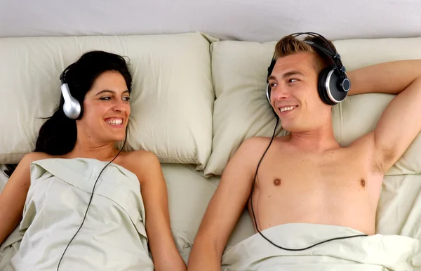 Young couple listening music to headphones on bed.