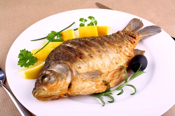 Fried carp on white plate with knife and fork