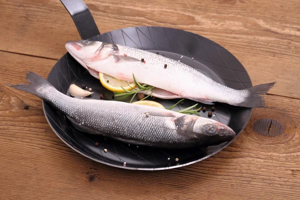 Two fresh sea bass fish on frying pan with lemon