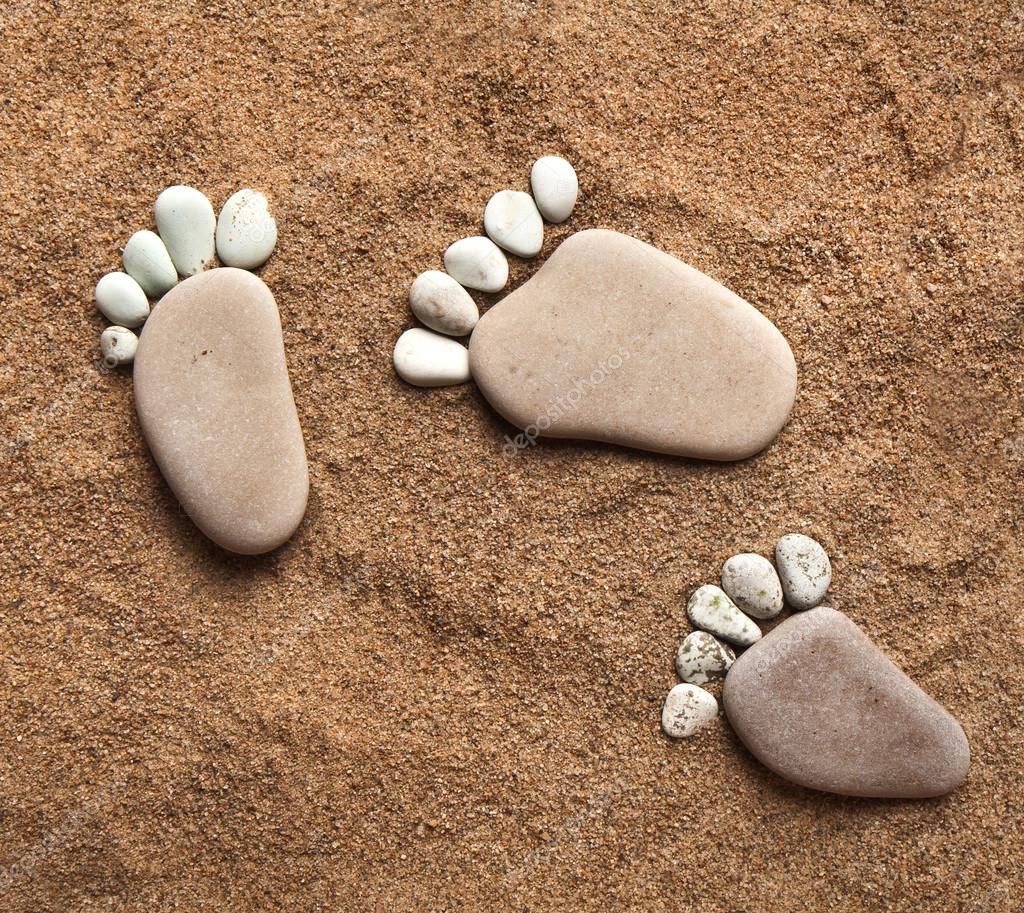 Trace bare feet walking made of pebble stones on the beach sand