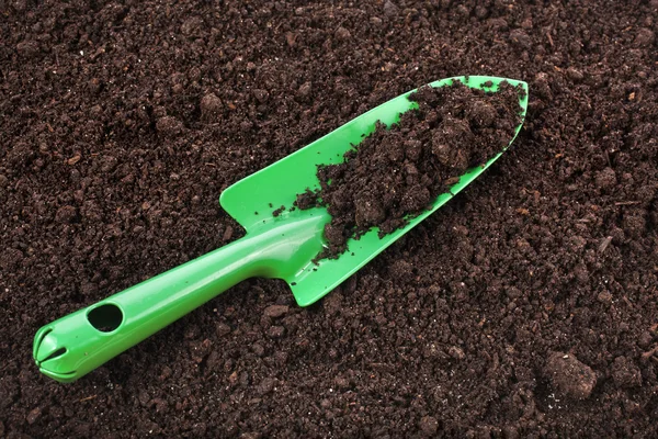 Close up of organic soil surface background and green gardening tool