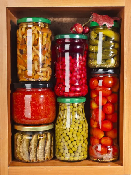 Many glass bottles with preserved food in wooden cabinet
