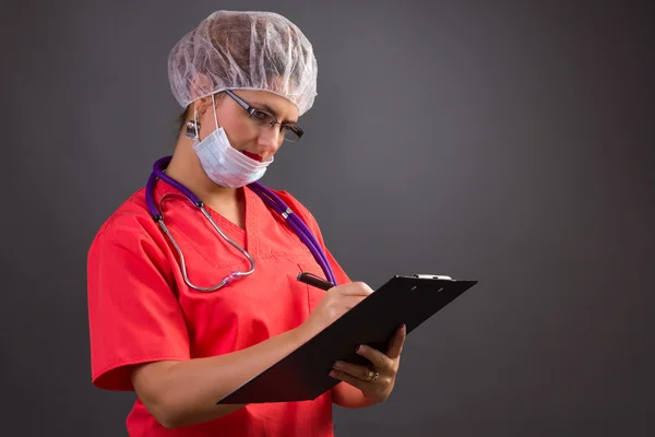 Female doctor with cap and mask writing on clipboard