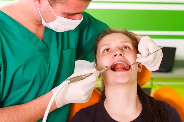 Young male dentist working, treating a young female patient.
