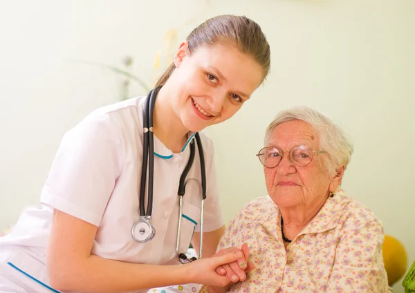Nurse visiting an elderly sick woman holding her hands with caring attitude.