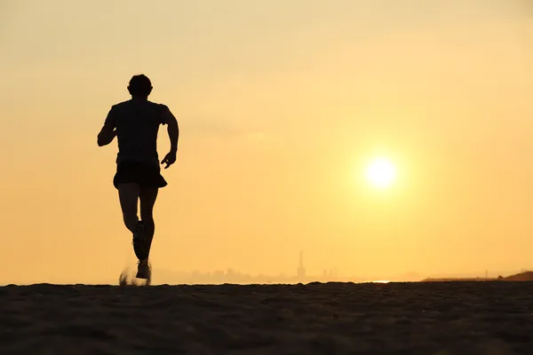 Back view of a man running on the beach at sunset