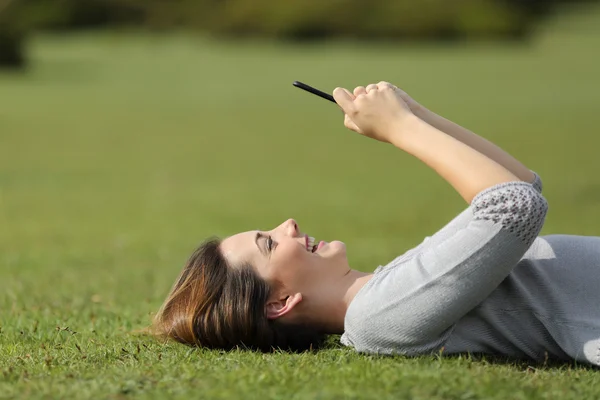 Woman using a smart phone resting on the grass in a park