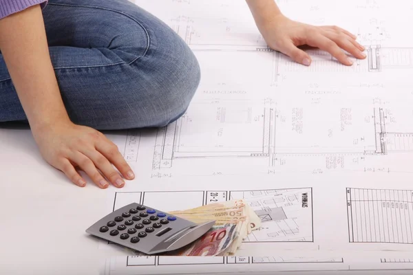 Woman with blueprint, helmet, calculators, money