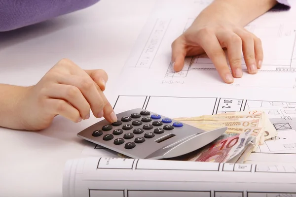 Woman with blueprint, helmet, calculators, money