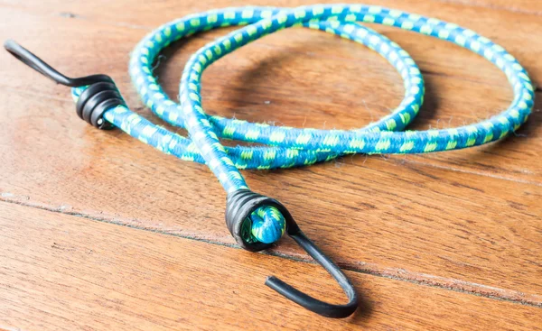 Blue elastic rope with metal hooks on wood background