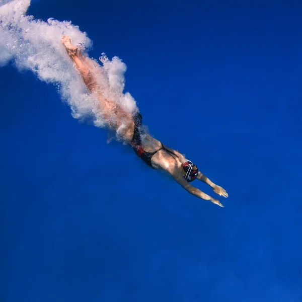 Professional female swimmer after jumping with air bubbles trail in blue water