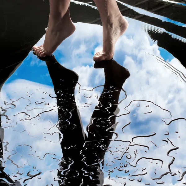 Walking wet barefoot on reflection of the sky in puddle