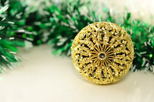 Christmas background with gold carved ball and green tinsel on white.