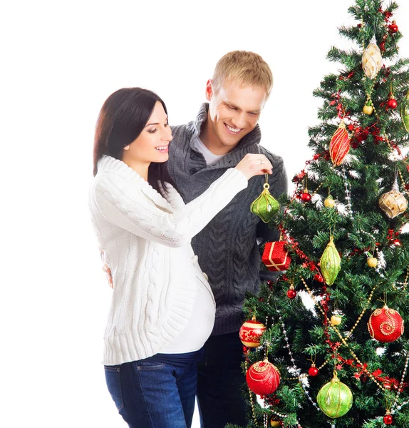 A pregnant woman and a happy man posing near the Christmas tree