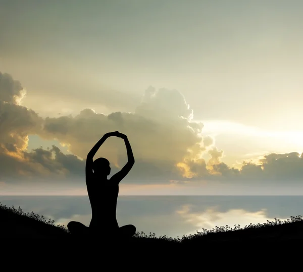 Silhouette of a young woman meditating on a sunset