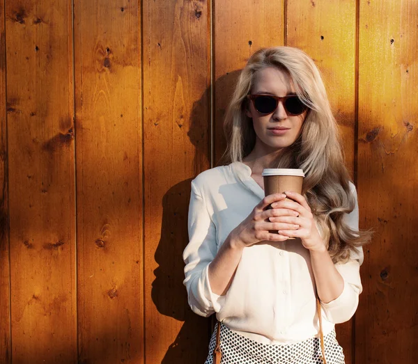 Young sexy blonde girl with long hair in sunglasses holding a cup of coffee have fun and good mood looking in camera and smiling evening soft sunlight, warm, tonning