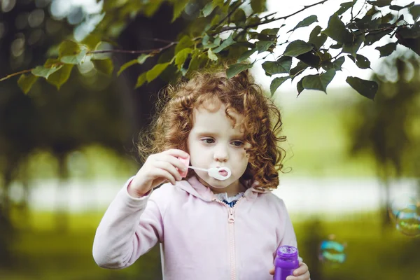 A little girl blowing soap bubbles, closeup portrait beautiful c