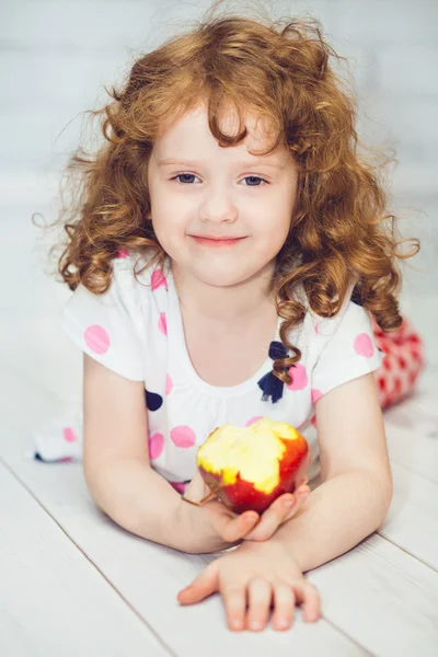 Curly girl smiling and eating a red apple