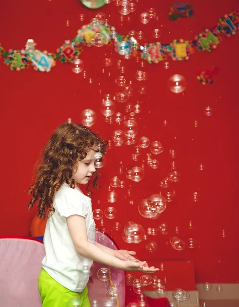 Curly girl catches soap bubbles with their hands.